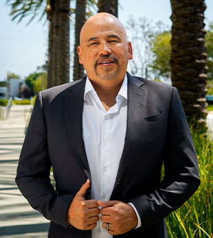 Mynor Arevalo, Regional Sales Manager at BluePoint Mortgage, standing confidently in a gray suit and orange tie, ready to support mortgage brokers nationwide.