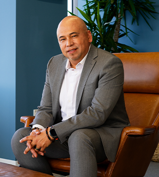 Mynor Arevalo, Regional Sales Manager at BluePoint Mortgage, standing confidently in a gray suit and orange tie, ready to support mortgage brokers nationwide.